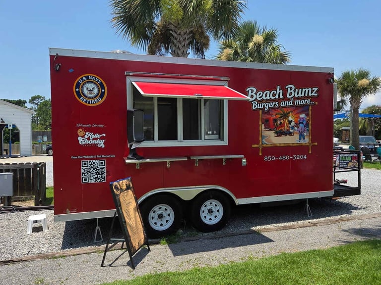 Red food truck with Beach Bumz logo and serving window, parked on grass with palm trees behind it